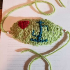 FRAN ENGLANDER
This is a mask I wove (using as the weft, netting that held Bonbel cheeses) and embroidered. The aqua symbol is a rune that stands for healing.