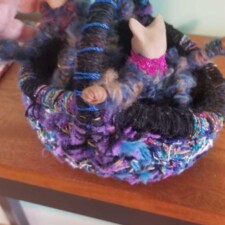JUDI MAGDER
Started stitching this small wicker basket with random yarn months ago..and put it aside..I couldn't readily figure out how to line it..it is only 4 inches across... when I got the unfinished challenge from LAFTA..I looked at it again..I stretched out a black sock and I cut off at the toe so I had a rounded knit shape that I sewed into the basket to make a lining. .worked great !! It turned out to be a perfect place for some yarn cats a made several years ago, so now it is a "Cat Nest".