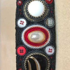 AMY SLOBODA
Here is my finished project- the ultimate procrastination. It is a cuff bracelet made from my mother’s clip on earrings and some buttons from her sewing box. I did most of the beading in relatively short order and then completely froze because I was afraid to trim away the edges. This sat for at least 5 years- maybe longer….despite Sandy Gudorf encouraging me and even sending me directions on how to finish it. Fear of failure was the root of it. I guess the final push was realizing just how ridiculous it was leaving it there undone- what good was it in the drawer? So, I took the plunge and actually really enjoyed the final step. Have not had a chance to wear it since we aren’t leaving the house :).