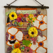 PORTIA BROWN
My art seeds made me smile right away- the little plastic frog, the Eveready Battery pin, and the bookmark proclaiming “The Earth Laughs with Flowers;” I immediately decided this was going to be fun and hopefully bring a smile to viewers. My first foray into stitching and fabric collage was in the LAFTA Professional Development Workshop started last year and cut short by Covid. The segment we didn’t get to was 3-D, so, I decided to try a “third dimension” in this piece. Not wanting to buy new materials or venture to stores, it was a challenge to find material in colors that worked with the seed materials; but, once I found the 50’s pop art material, I was on a roll. Tossing aside worries about lack of experience and depth of technique, I jumped blithely into seeing how many ways I could make cheery flower images: stuffed poppies, rough little rosettes from silk scraps, imitating composite flowers using old buttons & layers various fabric including wrapping paper ribbon and scraps of old silk, applique cut-out flowers, and few little embroidered daisies. At a time when there is so much that is discouraging, working with lightheartedness came as a welcome relief. I hope you are smiling!